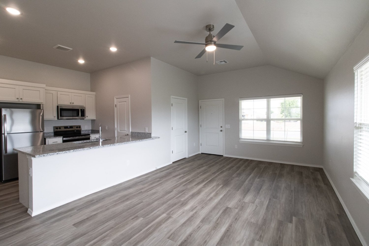 Open-concept kitchen with granite counters and a breakfast-bar peninsula, stainless appliances, and wood-look flooring